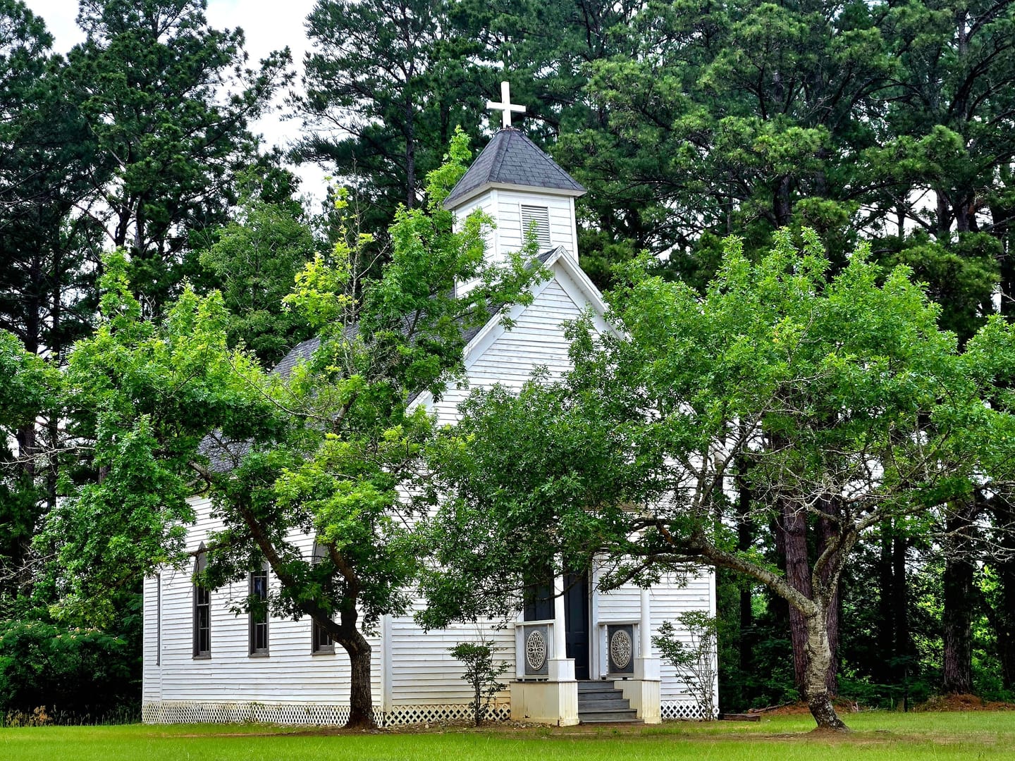 A white wooden church with a steeple among green trees: a licensed sample photo, not a real Example Community Church